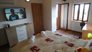 A bedroom with a bed, a TV on the wall, a wooden wardrobe, a door, and a window. - CASA BOZZERO, elegant and modern rustic with 2 apartments (Krnica)