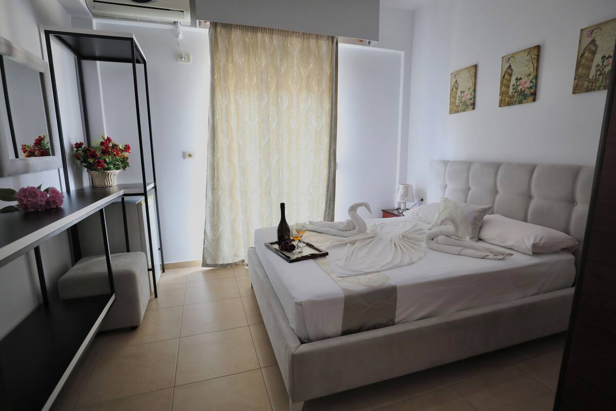 Habitación de hotel con una cama, un escritorio con un florero y un jarrón de flores, un espejo y obras de arte en la pared.
