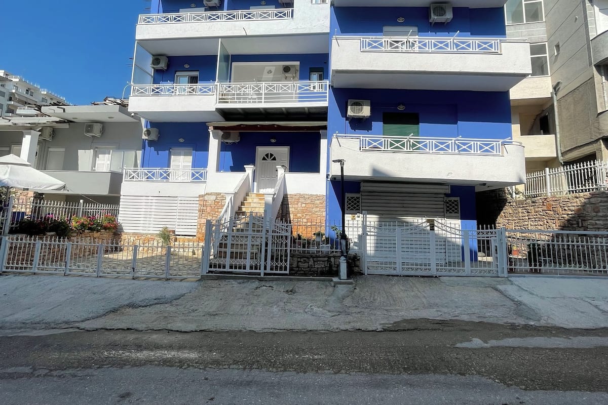 Un edificio de varios pisos con balcones, una entrada con reja y un cielo despejado.