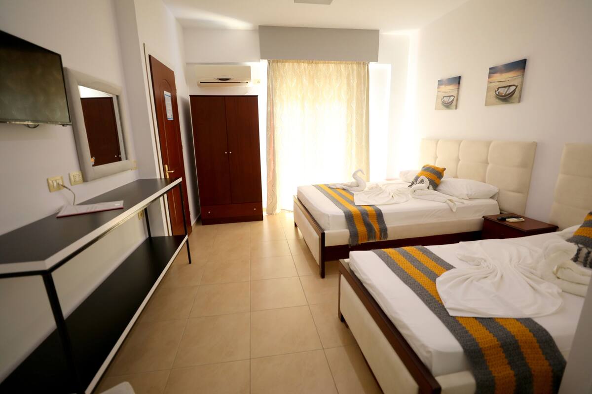 Habitación de hotel con dos camas, un escritorio, un televisor y una puerta que da a otra habitación.