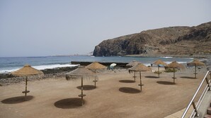 A beach with thatched umbrellas and a rocky cliff in the background. - Spacious and cozy apartment  (Palm-Mar)