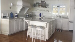 Een ruime keuken met witte kasten, een centraal eiland met krukken, en een raam dat voor daglicht zorgt.