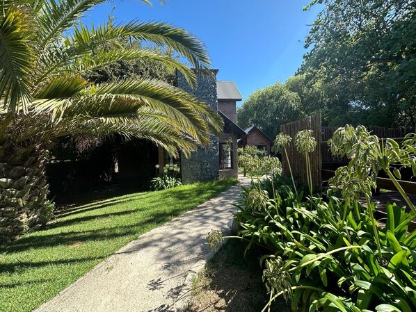 A pathway leading to a stone building with a brick roof, surrounded by lush greenery and a palm tree.
