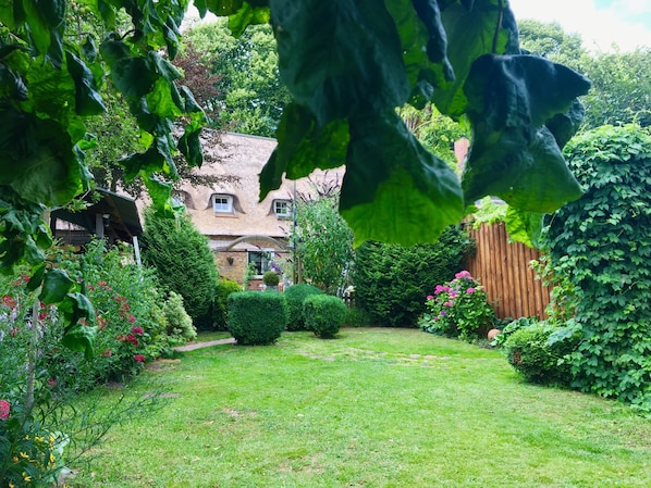 A well-maintained garden with a lawn, various plants, a wooden fence, and a house with a thatched roof. - Ferienwohnung Nr. 1-Apartment-Private Bathroom (Schwabstedt)