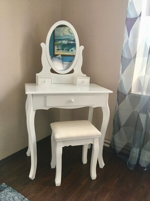 Une coiffeuse blanche avec un miroir, un petit banc et un tiroir.