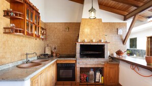 Een keuken met een inbouwoven, een dubbele spoelbak, houten kastjes en een hangende lamp.