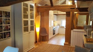 Una cocina acogedora con vigas de madera, un comedor con sillas de mimbre y vistas al salón.