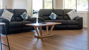 Ein modernes Wohnzimmer mit einem dunkelbraunen Ledersofa, einem Holztisch und einem großen Fenster, das für natürliches Licht sorgt.