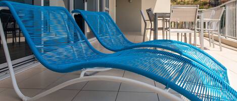 Un balcón con dos sillones azules, una mesa y una silla.