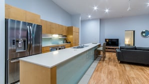 Una cocina moderna con electrodomésticos de acero inoxidable, una isla central y un área de comedor con sofá y televisor.