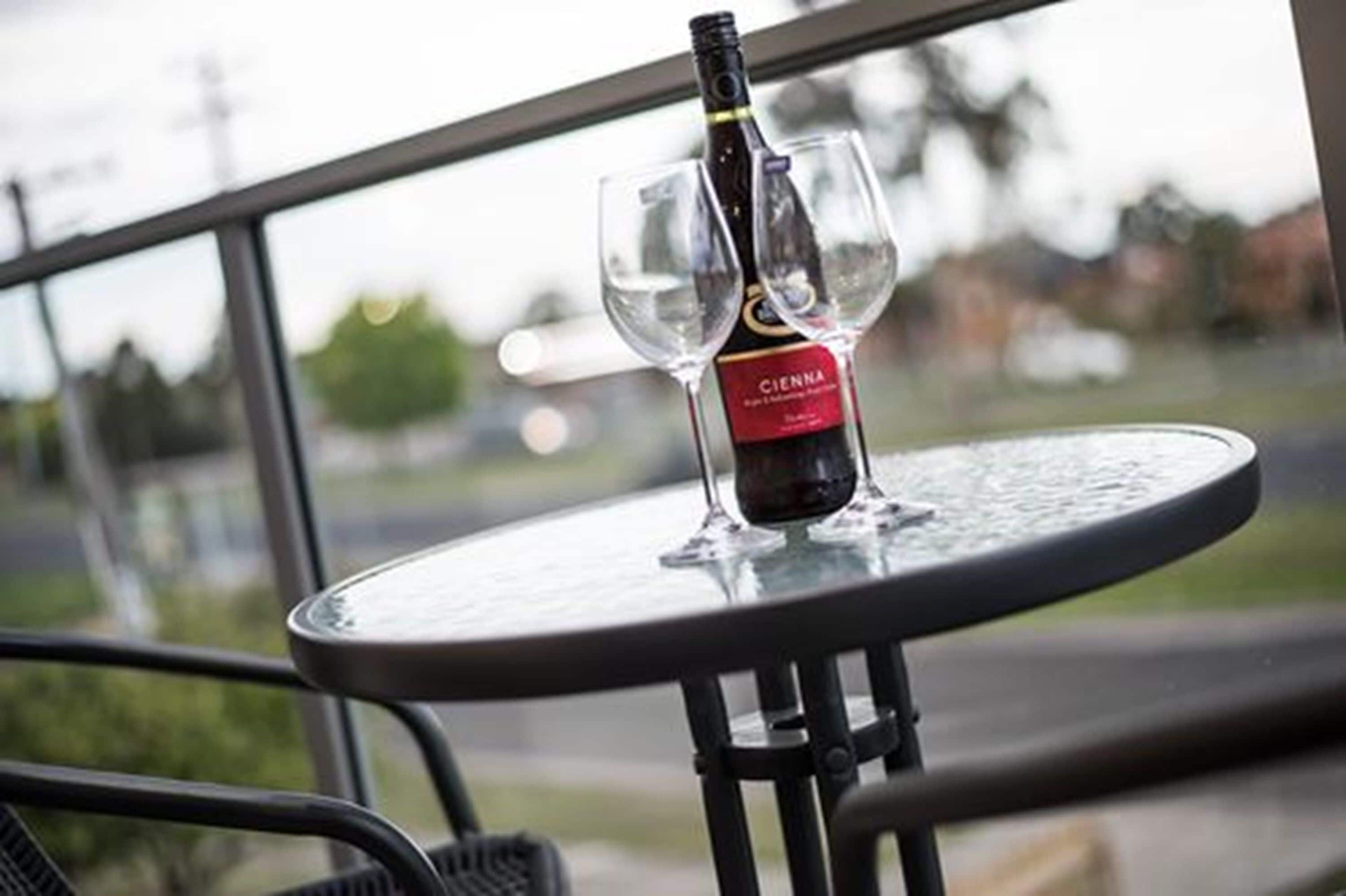 A bottle of Cienna wine on a glass table with a view of a road and greenery in the background.