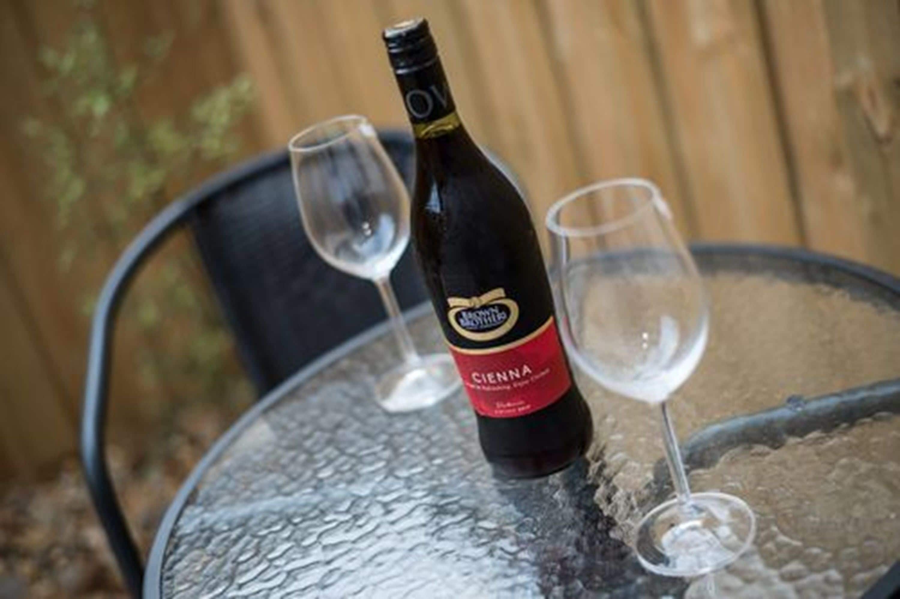 Una botella de vino sobre una mesa de vidrio con dos copas de vino vacías.