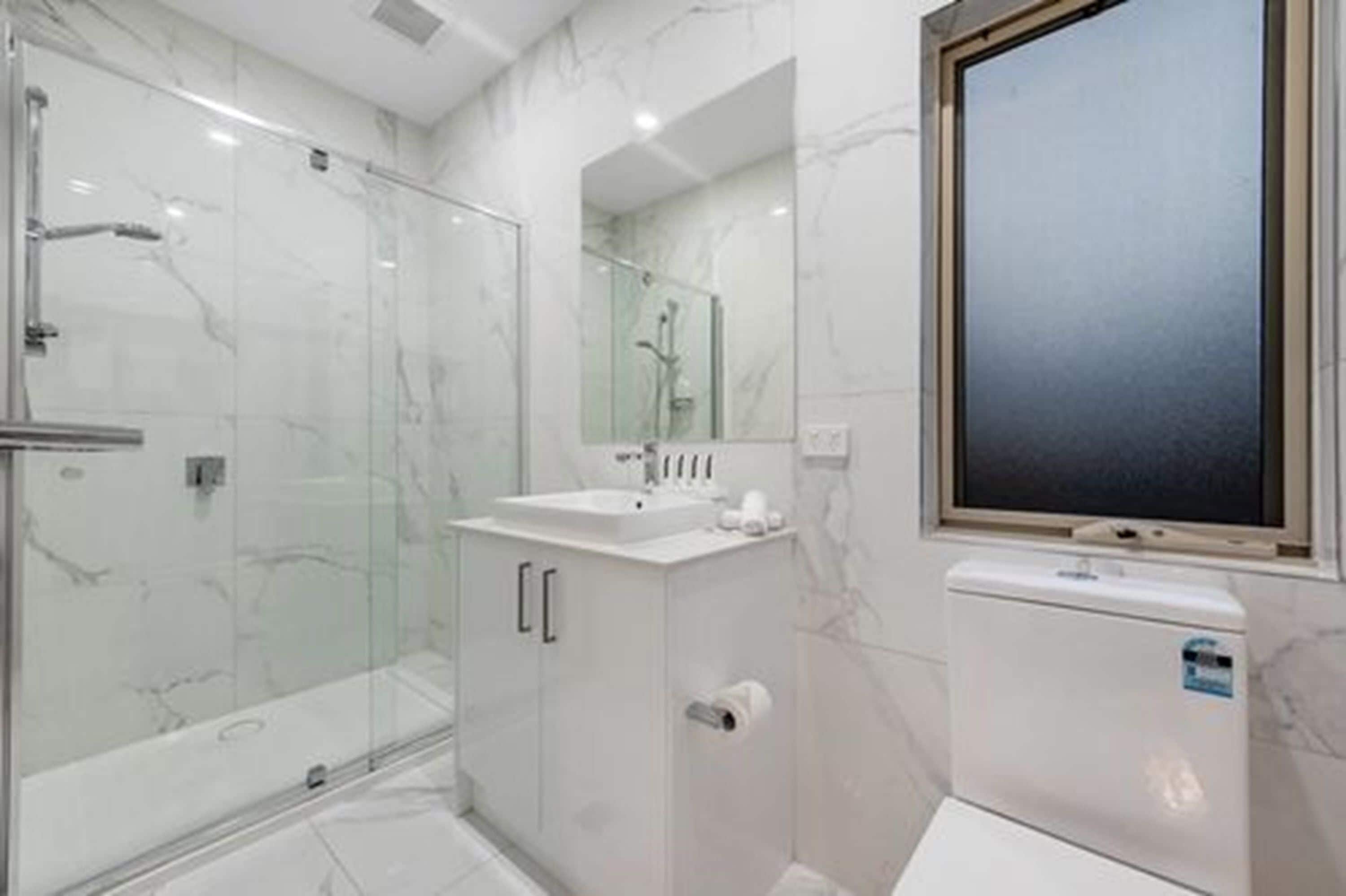 Un baño moderno con cabina de ducha de vidrio, un lavabo blanco y un espejo grande.