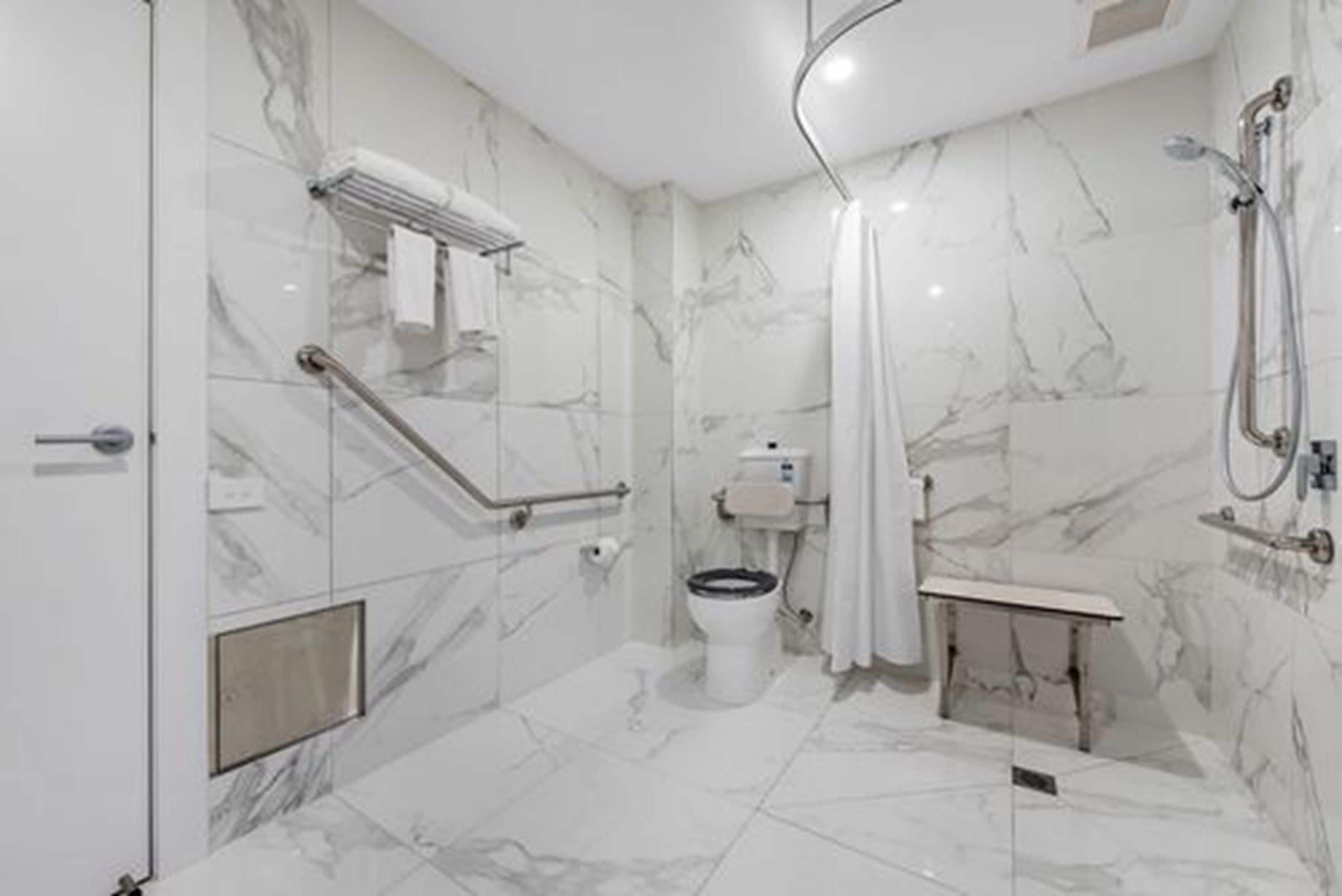 Ein modernes Badezimmer mit Marmorboden, Toilette, Dusche und Haltegriff.