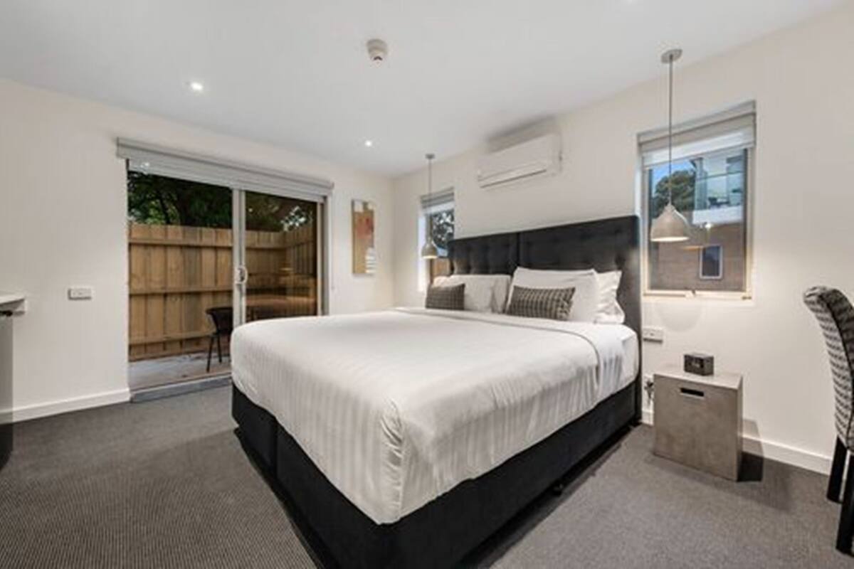 A modern bedroom with a large bed, a sliding glass door to the outside, and a small bedside table.