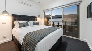 Moderni hotellihuone, jossa on suuri sänky, parvekkeelle johtava liukuovi ja seinälle asennettu taulutelevisio.