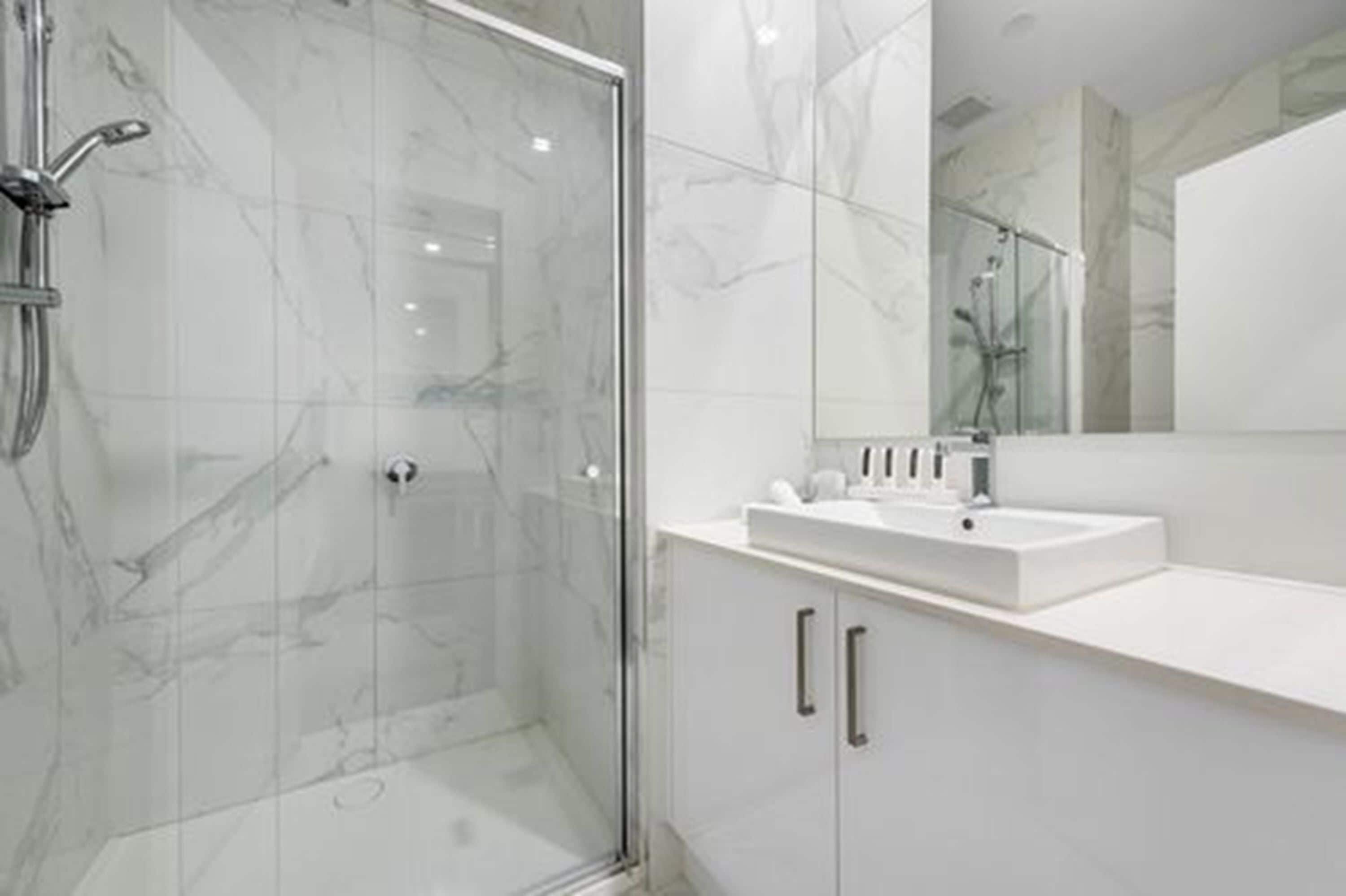 A modern bathroom with a glass-enclosed shower, a white sink, and a large mirror.