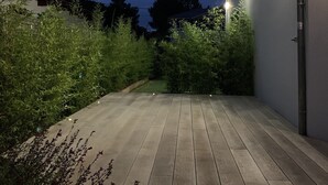 Un terrazzo in legno con vista su un edificio moderno e vegetazione circostante.