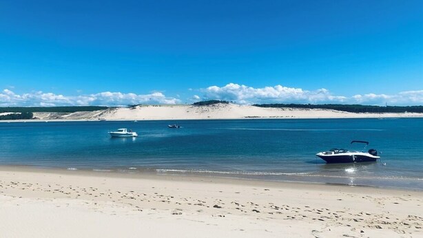 Una spiaggia con due barche, un litorale sabbioso e una collina in lontananza.