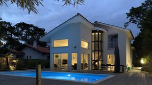 Una moderna casa a due piani con piscina, ampie finestre e una veranda coperta.