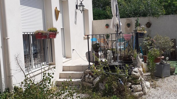 Ein Gebäude mit weißer Fassade, einem Balkon mit Blumentöpfen, einer Statue und einem Kiesweg.