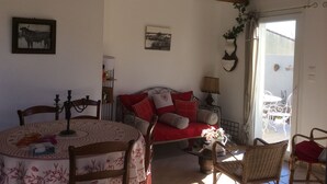 Ein gemütliches Wohnzimmer mit Holzbalkendecke, einem Esstisch mit Stühlen, einer Couch mit roten Kissen und einer Deckenleuchte.