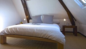Un dormitorio con techo inclinado, estructura de cama de madera, colchón blanco y dos mesitas de noche con lámparas.