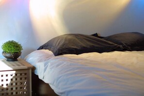 A bed with white bedding and two dark pillows, a small potted plant on a side table, and a wooden headboard. - Air conditioned duplex in a 19th century mansion centrally located with parking (Tours)