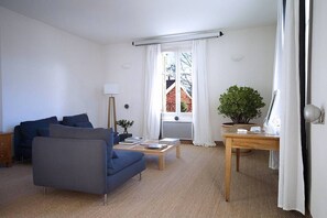 A modern living room with a blue sofa, a wooden coffee table, a desk with a computer, and a window with white curtains. - Air conditioned duplex in a 19th century mansion centrally located with parking (Tours)