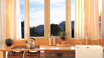A kitchen with a wooden countertop, a stainless steel kettle, a fruit bowl, and a sink.