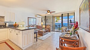 A spacious kitchen with a central island, a dining area with wicker chairs, and a balcony with a view of the ocean.