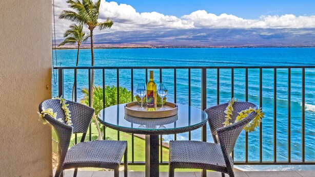A balcony with a round glass table, two wicker chairs, a bottle of wine, and a glass on the table.