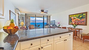 A kitchen with a large island, a dining area with a view of the ocean, and a ceiling fan.