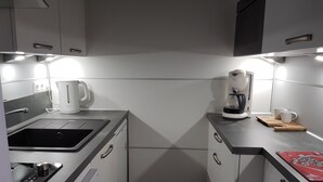 Una cocina compacta con estufa integrada, cafetera y hervidor.