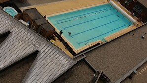 Vista aérea de una piscina con carriles, rodeada de edificios y una zona cubierta con techo.