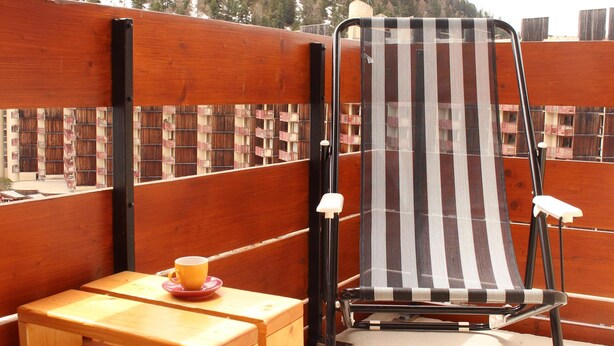 Una mesa de madera y una silla a rayas en un balcón con vistas a un paisaje montañoso.