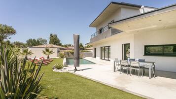 Een modern huis met een zwembad, een terras met tuinmeubilair en een verzorgd gazon.