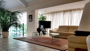 Ein modernes Wohnzimmer mit einer Couch, einem Couchtisch, einem Fernseher und einer großen Topfpflanze.