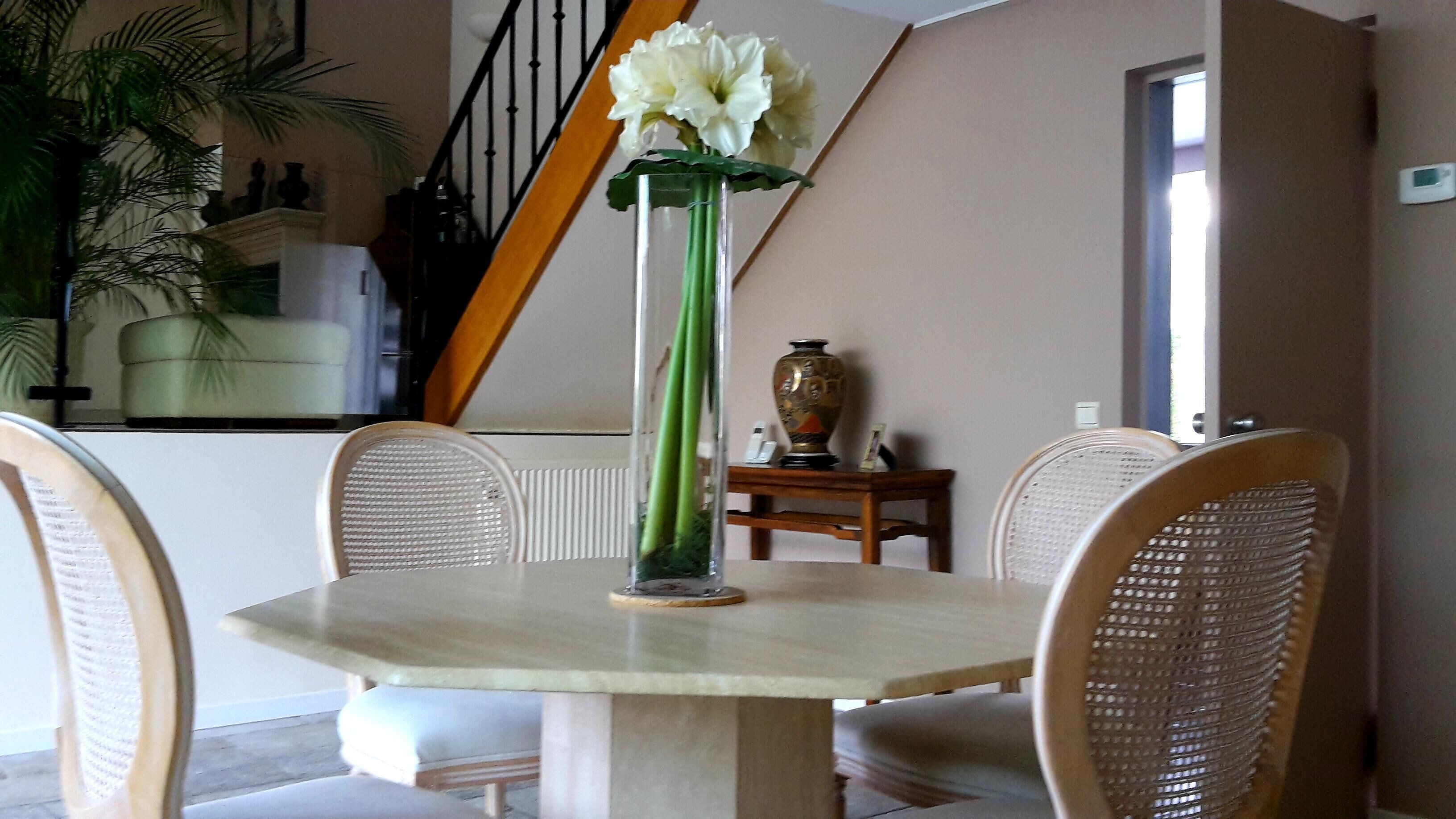 Une table à manger ornée d’un vase de fleurs, entourée de chaises en osier.