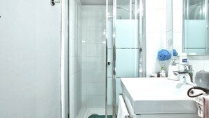 Een moderne badkamer met een glazen douchecabine, een witte wastafel en een spiegel.
