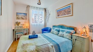 Een slaapkamer met een bed, een bureau, een stoel, een nachtkastje en een lamp.