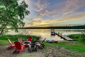 Un paisaje junto al lago con un muelle, una mesa con sillas y un bote.