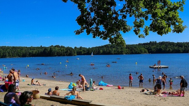 A beach with people sunbathing and swimming, a sailboat, and a dock with people on it. - The little log with a view of the lake (Marcillac-La-Croisille)