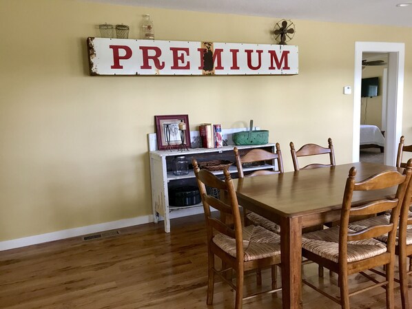 Un comedor con una mesa y sillas de madera, un estante con varios objetos, y un cartel que dice 'PREMIUM' en la pared.