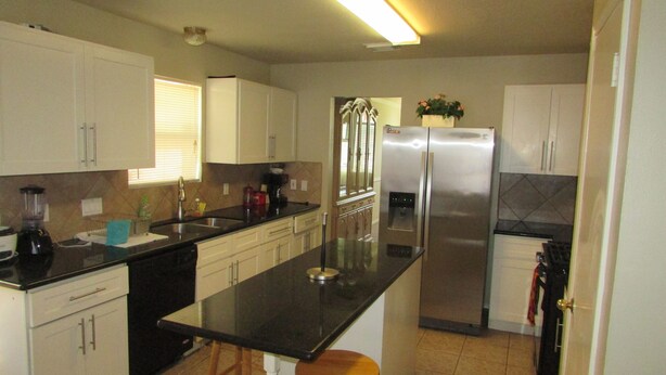 A kitchen with white cabinets, a black countertop, a stainless steel refrigerator, and a window with blinds. - Houston Near Stadium, Galleria and Downtown (Houston)