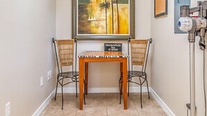 A hallway with a tiled floor, two wicker chairs, a wooden table, a framed painting, and a blue door.