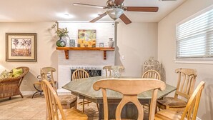 A dining area with a round table, wooden chairs, a ceiling fan, and a fireplace.