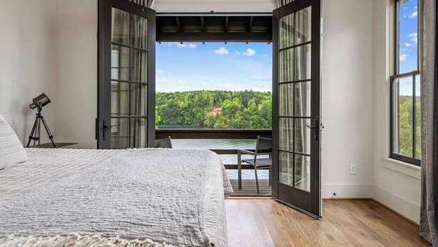 A bedroom with a large bed, a desk, and a view of a forest through open doors. - Modern Lake House on Smith Lake, AL close to Birmingham and Huntsville (Bremen)