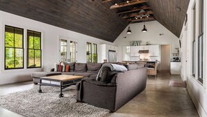 A spacious living room with a large sectional sofa, a coffee table, and a rug. There is a kitchen in the background with white cabinets and a dining area. - Modern Lake House on Smith Lake, AL close to Birmingham and Huntsville (Bremen)