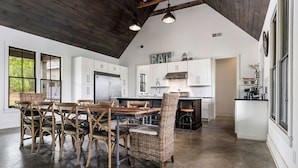 A spacious kitchen with white cabinets, a central island, and a dining area with wicker chairs. - Modern Lake House on Smith Lake, AL close to Birmingham and Huntsville (Bremen)